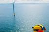 The image shows a worker surveying a wind turbine