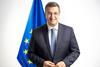 The image is of Commissioner Tzitzikostas standing in front of the EU flag