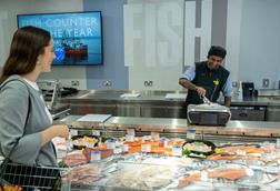 A shopper at a Waitrose fish counter with an employee weighing a seabass