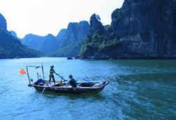 Vietnamese fishing boat with two fishers and cliffs in the background