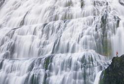 Very small person in red looking at a large waterfall