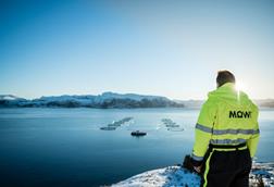 A worker dressed in a yellow high vis jacket is pictured overlooking a Mowi offshore fish farm