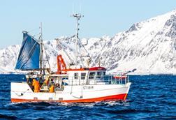 The image shows a Norwegian fishing vessel on the water with the snowy coastline in the background