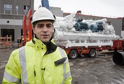 Arild Vikan, project manager at Salmon Evolution, in hi viz and hard hat standing in front of a heat pump being transported on a lorry