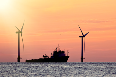 The image shows a vessel at sunset with wind turbines in the background