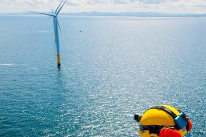 The image shows a worker surveying a wind turbine