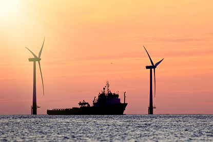 The image shows a vessel at sunset with wind turbines in the background