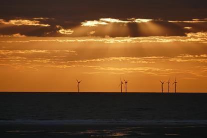 The image shows a generic image of offshore wind turbines at sunset