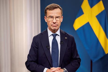 The image shows the ​the Swedish Prime Minister, Ulf Kristersson, pictured in front of a Swedish flag